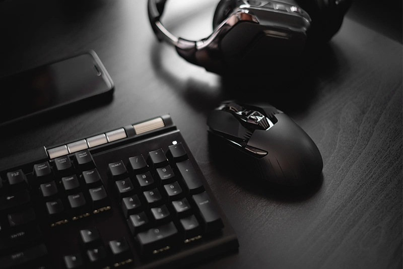 Black keyboard, gaming mouse, headset and smartphone arranged on a dark desk.